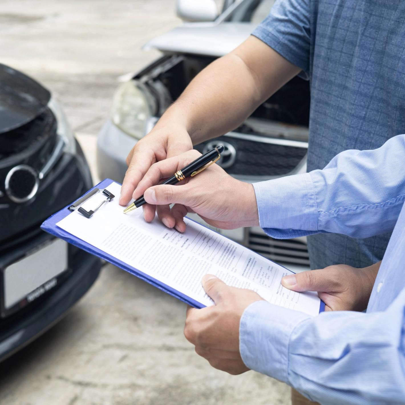 Persona scrive su modulo con auto danneggiata sullo sfondo.